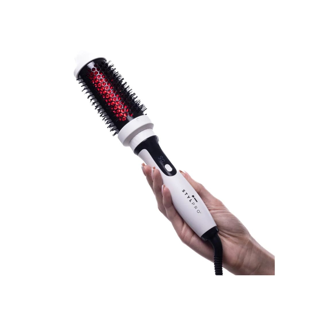 A hand holding a white and black round hairbrush hot air styler with red heating elements visible on the brush barrel, against a plain white background.