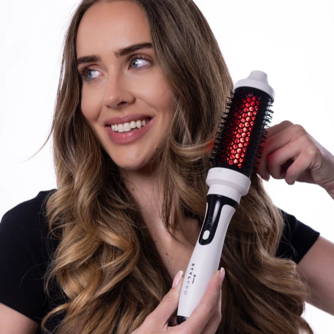 Woman using a hair styling tool with red heating elements on a white background