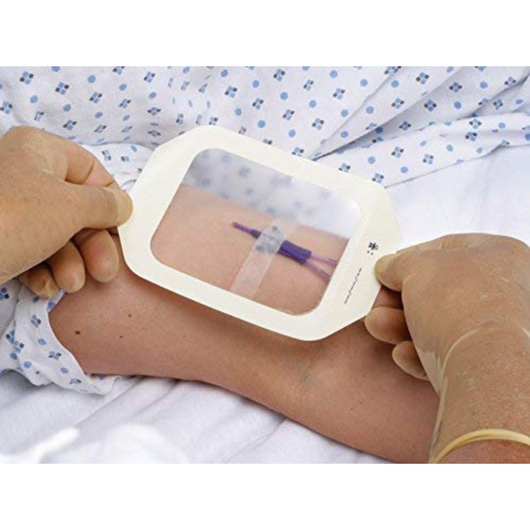 A close-up of a healthcare worker holding a clear, square medical monitoring pad over a patient's arm, with the patient wearing a blue and white patterned hospital gown.