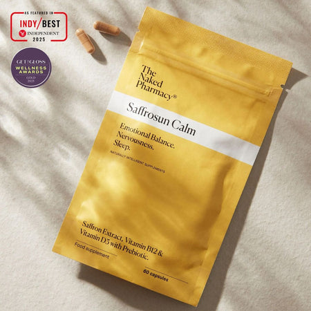 A gold stand-up pouch of Saffrosun Calm dietary supplement by The Naked Pharmacy, displayed on a textured light beige fabric background with two capsules nearby and award badges in the top-left corner.