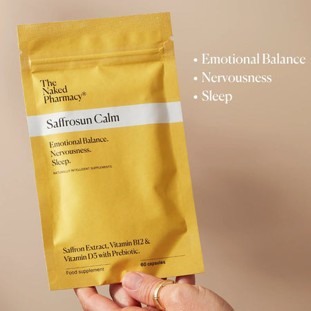 A hand holds a metallic gold stand-up pouch of The Naked Pharmacy Saffrosun Calm food supplement against a warm beige background. White text on the right lists benefits: Emotional Balance, Nervousness, and Sleep.