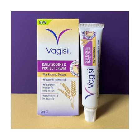 Vagisil Daily Soothe & Protect Cream shown with its retail box and squeeze tube on a beige surface against a purple background.