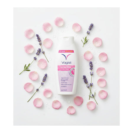 A bottle of Vagisil Ultra Polish hand cream is arranged in a flat lay on a white background, surrounded by pink rose petals, lavender sprigs, and water droplets.