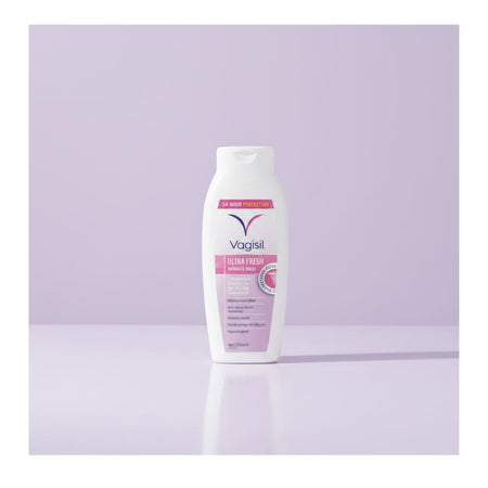 A bottle of Vagisil Ultra Strength Softener Body wash, white plastic bottle with pink and purple label details, standing on a light lavender reflective surface against a matching lavender background.