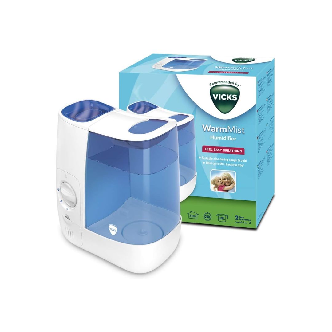 A Vicks WarmVist Humidifier shown in front of its retail packaging box on a clean white background. The humidifier is white with a translucent blue water tank and blue top tray.