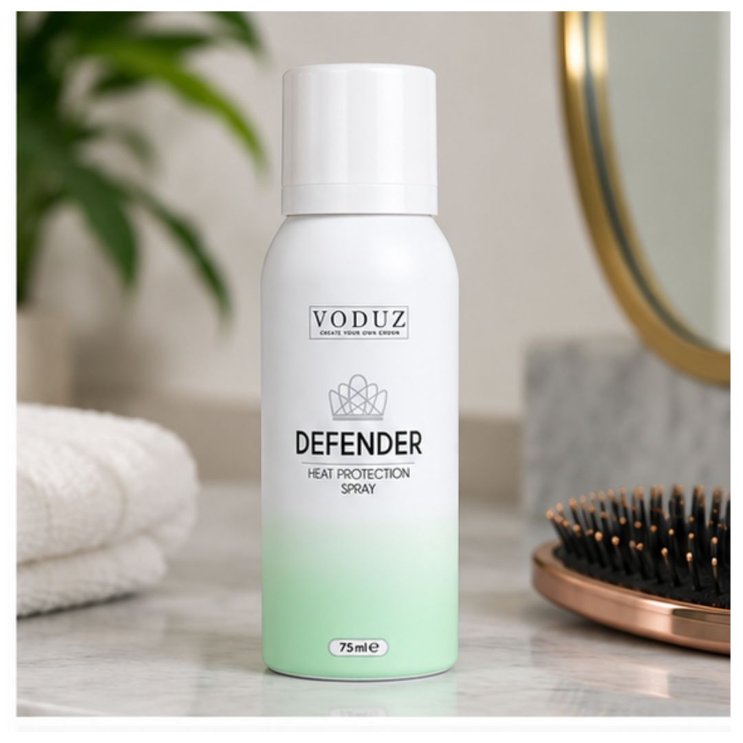 A 75ml can of VODUZ Defender Heat Protection Spray, featuring a white and mint green gradient design, set on a marble countertop with a towel, plant, and hairbrush in a blurred bathroom background.