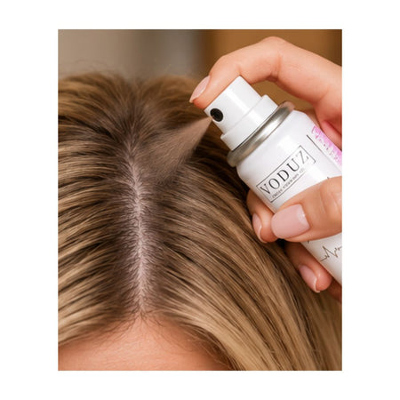 A close-up of a person's hair part being sprayed with a white VODUZ hair product from a hand-held pump bottle.