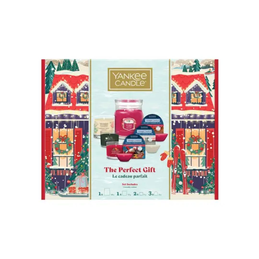 Yankee Candle 'The Perfect Gift' advent calendar set, featuring a festive holiday illustration of snow-covered houses on the sides and a central display of various candle products including a large jar candle and smaller tins.
