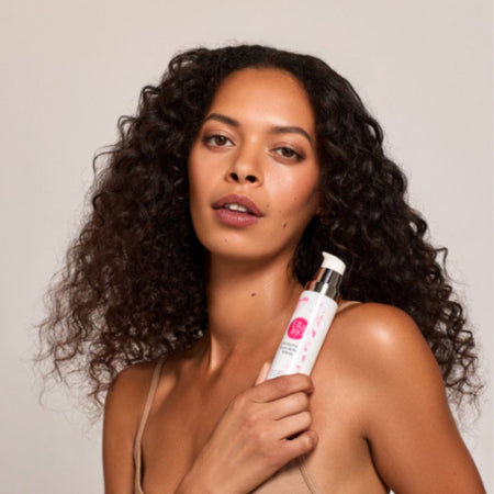 Woman holding a skincare product against a plain background